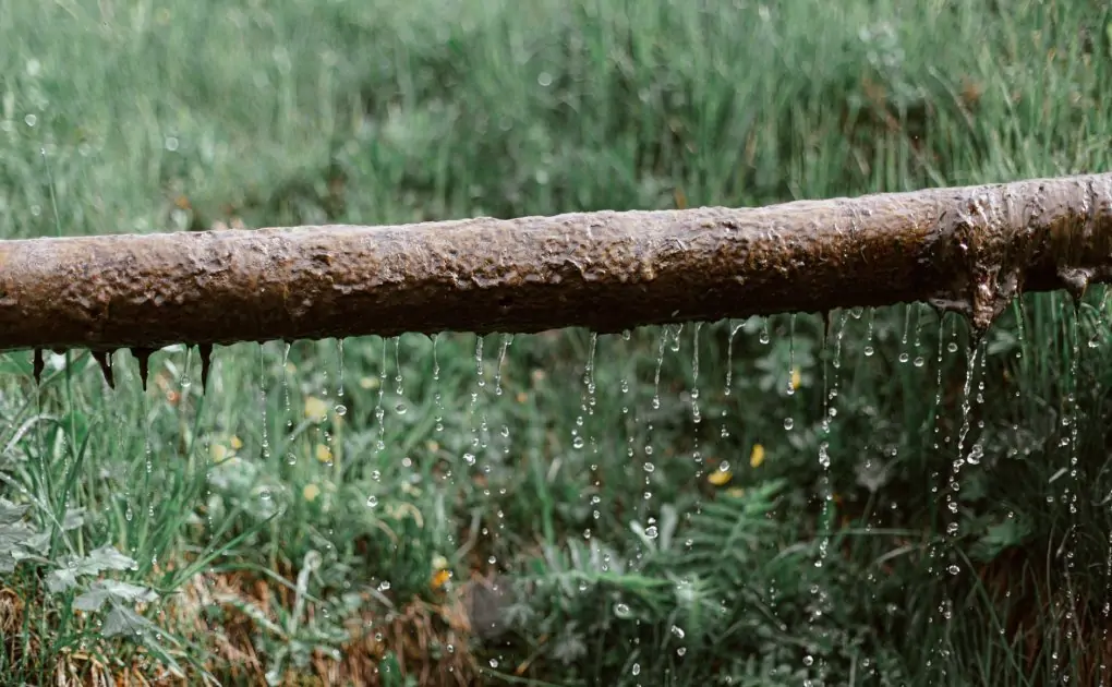 rusted metal leaking pipe above grassy meadow